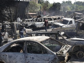 People look for salvageable pieces from burned cars at a mechanic shop that was set on fire during violence by armed gangs in Port-au-Prince, Haiti, Monday, March 25, 2024.