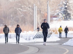 A jogger runs past heaps of snow along the pathway near the Bow River in Calgary on Sunday, March 24, 2024. Environment Canada is forecasting more snow starting April 3.