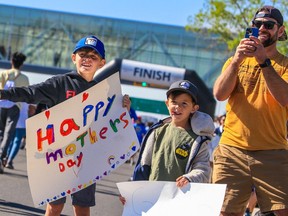 Henry, 8, and Theo, 5, cheer on their mom with their dad as she heads for the finish line in the 2023 Sport Chek Mother's Day Run near Chinook Centre on Sunday, May 14, 2023.