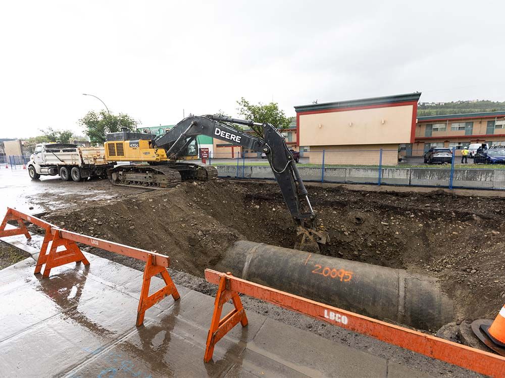 An excavator works around a length of exposed water feeder main on 16 Avenue N.W. between 45 and 46 Streets in Calgary on Tuesday, June 18, 2024. The segment was one of five weak points identified in the water pipeline following a major break earlier in June.