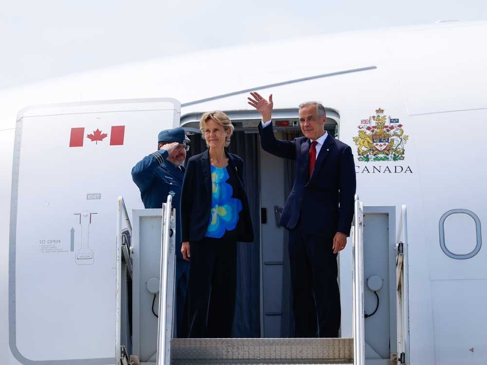 Prime Minister Mark Carney joined by his wife Diana Fox Carney waves before boarding a plane in Ottawa on Monday, July 6, 2026.