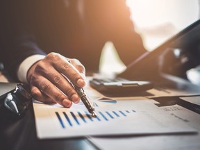 Close up Businessman consultant holding pen and pointing at financial on wooden desk in coffee shop. freelance, tax, accounting, statistics and analytic research concept.