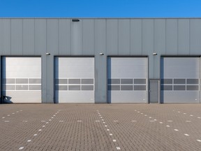 A row of grey industrial units with roller shutter doors. Industrial is a promising area for investing in commercial real estate right now, according to industry insiders. Demand is up and rents are rising.