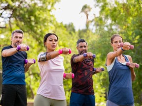 Two men and two women exercise using dumbbells at park. Men and women seek help with health and wellness in different ways.