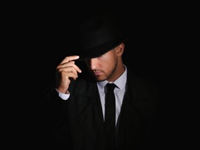 An old-fashioned male detective wearing a hat in a Noir setting with dark background. One espionage-themed immersive travel experience includes being coached on surveillance, escape and combat by former intelligence officers.