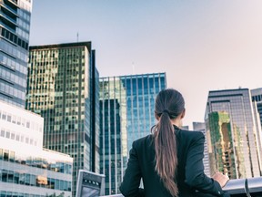 Businesswoman from the back contemplating downtown office-building skyline. Over the long-term, property acts as a hedge against inflation, HNW investors find