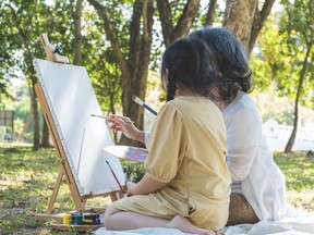 Back view of an older woman shows a child how to paint on an easel set up in a park. This strategy is ‘not a short-term investment strategy. It’s really something long-term that you want to put in place to transfer assets from one generation to the other,’ says one expert.