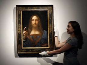 FILE- In this Oct. 24, 2017 file photo, an employee poses with Leonardo da Vinci's "Salvator Mundi" on display at Christie's auction rooms in London. An official in the United Arab Emirates says the new Louvre museum in Abu Dhabi is "very proud" to have acquired a painting by Leonardo da Vinci that sold for a staggering $450 million last month.(AP Photo/Kirsty Wigglesworth, File)