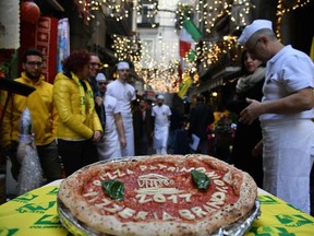 Neapolitan pizza makers show a pizza celebrating the Unesco decision to make the art of Neapolitan "Pizzaiuolo" an "intangible heritage", on December 7, 2017 outside the Pizzeria Brandi in Naples.   The art of the Neapolitan Pizzaiuolo is a culinary practice consisting of four different phases relating to the preparation of the dough and its baking in a wood-fired oven. The practice originates in Naples, where around 3,000 Pizzaiuoli now live and  perform, and plays a key role in fostering social gatherings and intergenerational exchange.