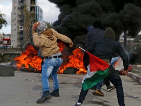Palestinian demonstrators holding a national flag throw stones towards Israeli troops during clashes that followed protests against a decision by US President Donald Trump to recognise Jerusalem as the capital of Israel, in the West Bank city of Ramallah on December 7, 2017.