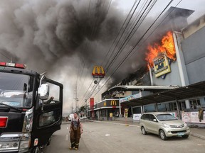 This photo taken on December 23, 2017 shows a firefighter standing in front of a burning shopping mall in Davao City on the southern Philippine island of Mindanao.  Thirty-seven people were believed killed in a fire that engulfed a shopping mall in the southern Philippine city of Davao, local authorities said on December 24.