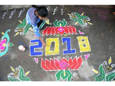 A woman applies coloured powder to a "rangoli", a Hindu ritual design, to usher in the New Year in front of a home in Hyderabad on January 1, 2018.  Rangolis are drawn in front of homes early in the morning to welcome relatives and friends to mark the New Year.