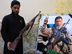 In this Tuesday, Dec. 5, 2017 photo, Talib, the son of Iraqi sniper Ali Jayad al-Salhi, poses with a weapon next to his father's poster in his home in Basra, Iraq.
