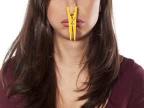 In this stock photo, a disgusted young woman pinches her nose with a clothespin.