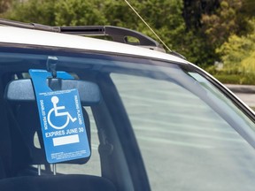 In this stock photo, a disabled parking permit hangs in the windshield of a car in a parking lot.