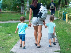 In this stock photo, a young woman walks two boys to school while carrying a backpack.