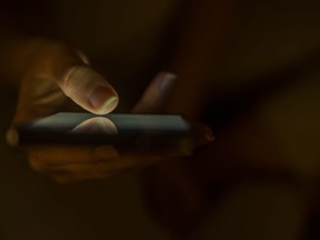 In this stock photo, a women looks at a cellphone in a dark room.