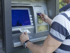 In this stock photo, a man takes cash from an ATM while holding a bank card.
