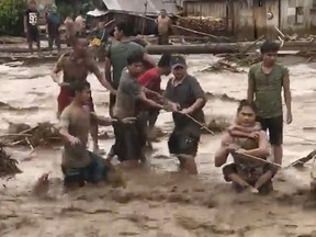 In this photo made from video by Aclimah Disumala, Friday, Dec. 22, 2017, villagers cross raging flood waters in Lanao del Norte, Zamboanga Pennisula, southern Philippines. A tropical storm has unleashed flash floods and set off landslides in the southern Philippines leaving dozens of people dead.