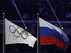 In this Feb. 23, 2014 file photo, the Russian national flag, right, flies next to the Olympic flag during the closing ceremony of the 2014 Winter Olympics in Sochi, Russia. (AP Photo/Matthias Schrader, File)