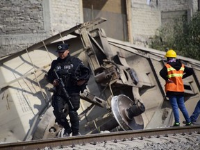 Security forces and railroad workers stand at the site where the last car of freight train derailed, hit two houses and killed five people in the municipality of Ecatepec, just north of Mexico City, on January 18, 2018. Only the last wagon, which was carrying corn, went off the tracks.