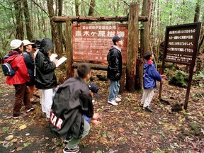 In this Thursday, Oct. 22, 1998, file photo a group of schoolchildren read signs posted in the dense woods of the Aokigahara Forest at the base of Mount Fuji, Japan. (AP Photo/Atsushi Tsukada, File)