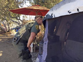 An Orange County sheriff's deputy calls to residents inside a tent in Anaheim, Calif., Monday, Jan. 22, 2018.
