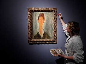 In this photo taken on March 15, 2017, a woman puts the finishing touches on the painting Ritratto di Chaim Soutine ' (Portrait of Chaim Soutine), attributed in the exhibit to the Italian painter Amedeo Modigliani, on display at the Ducal Palace in Genoa, Italy. Consumer advocates are demanding refunds after an expert ruled that a Genoa exhibit was full of Modigliani fakes. (Luca Zennaro/ANSA via AP)