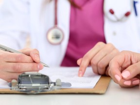 In this stock photo, a female doctor fills out a form on a clipboard.