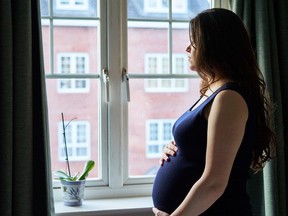 In this stock photo, a pregnant woman looks out of a bedroom window.