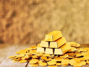 This stock photo shows gold bars and coins on wooden table.