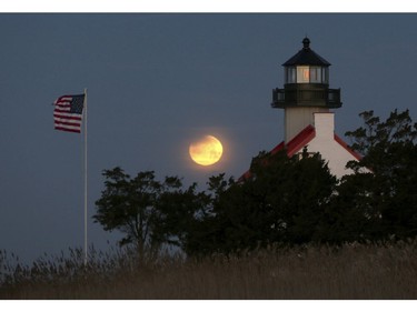 Earth's shadow begins to cross the upper left of the full moon Wednesday Jan.  31, 2018, as it sets in the west behind the East Point Lighthouse in Cumberland County, N.J. (Dale Gerhard/The Press of Atlantic City via AP)