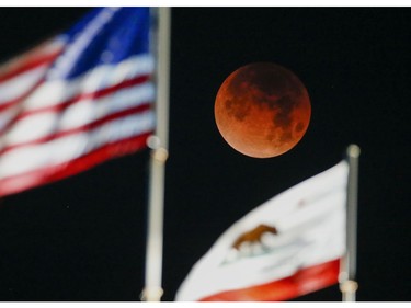 A rare occurrence called a 'Super Blue Blood Moon' is seen behind the flags of U.S. and California State at Santa Monica Beach in Santa Monica, Calif., Wednesday, Jan. 31, 2018. (AP Photo/Ringo H.W. Chiu)