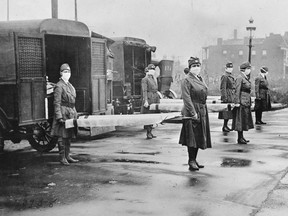 In this October 1918 photo made available by the Library of Congress, St. Louis Red Cross Motor Corps personnel wear masks as they hold stretchers next to ambulances in preparation for victims of the influenza epidemic. A century after one of history's most catastrophic disease outbreaks, scientists are rethinking how to guard against another super-flu like the 1918 influenza that slaughtered tens of millions as it swept the globe in mere months.   (Library of Congress via AP)