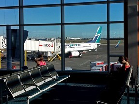 Passengers wait for a flight in the Vancouver International Airport terminal with a WestJet 737-700 seen out the window on Sept. 20, 2014.