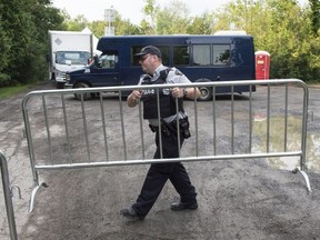 An RCMP officer moves a barricade as they wait for the arrival of asylum seekers crossing the border into Canada from the United States at a police checkpoint close to the Canada-U.S. border near Hemmingford, Que., on Thursday, August 3, 2017.