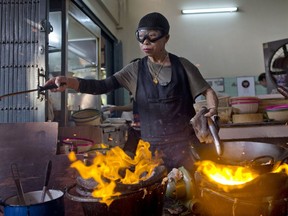 In this Dec. 20, 2017, photo, Thai cook Supinya Jansuta, 72, better known as "Jay Fai," wearing goggles, cooks with two flaming woks at her eatery in Bangkok, Thailand. After spending more than three decades cooking in an unassuming outdoor kitchen, Jay Fay has been propelled to international culinary stardom by having her restaurant awarded a Michelin star.