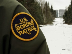 A U.S. Border Patrol agent stands along the boundary marker cut into the forest marking the line between Canada on the right and the United States on March 23, 2006 near Beecher Falls, Vermont.