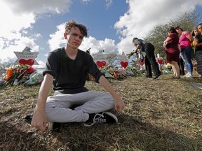 Chris Grady, a student at Marjory Stoneman Douglas High School, poses at a memorial outside the school, for Wednesday's mass shooting, in Parkland, Fla., Monday, Feb. 19, 2018. Grady huddled in his classroom at the high school last Wednesday listening to shots ring out nearby, what he felt wasn't fear, but anger. Grady and his friend are among about 100 Stoneman Douglas students who are heading to Florida's capital, Tallahassee, to push lawmakers to do something to stop gun violence.