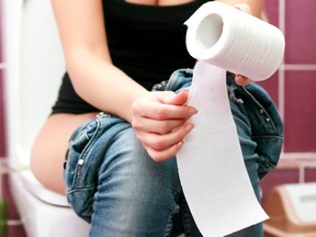 In this stock photo, a woman sits on a toilet in a public washroom.