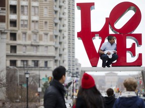 FILE - In this March 27, 2015, file photo, a young man climbs on artist Robert Indiana's LOVE sculpture in John F. Kennedy Plaza, also known as Love Park, in Philadelphia. The sculpture, temporarily relocated in 2016 before renovations to the plaza, is set to return to its traditional location Tuesday, Feb. 13, 2018, ahead of Valentine's Day. The tourist attraction has been repainted to its original colors and will be installed on a new rectangular pedestal, in keeping with how Indiana's other works are displayed.