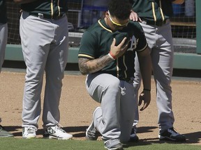 In this Sunday, Oct. 1, 2017 file photo, Oakland Athletics catcher Bruce Maxwell takes a knee during the national anthem next to teammates Mark Canha, right, and Raul Alcantara in Arlington, Texas.