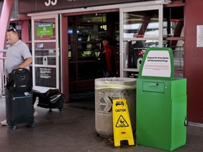 Unidentified travelers exit the airport past a green metal container designed for "Disposal for Prescription and Recreational Drugs," set outside one of the entrances to McCarran International Airport in Las Vegas, Thursday, Feb. 22, 2018. People catching a flight at the airport can now get rid of prescription and recreational drugs, before entering the Clark County-Department of Aviation-owned property, thanks to the receptacles commonly referred to as "amnesty boxes." The first of about 20 green metal containers commonly referred to as amnesty boxes were installed earlier this month in response to county officials banning marijuana possession and advertising at the airport last year.