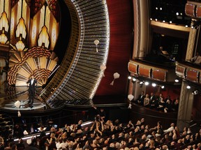 FILE - In this Feb. 26, 2017 file photo, host Jimmy Kimmel speaks as donuts fall onto the audience at the Oscars in Los Angeles. Cameras never find an empty seat at the Academy Awards, with a troop of seat-fillers at the ready to occupy any chair vacated by a bathroom- or bar-bound guest. A parade of extras in tuxedoes and gowns arrive hours before the show begins and are ready to swoop in and sit once the cameras start rolling.