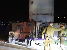 Israeli security forces walk next to a military jeep that was damaged when a Palestinian assailant rammed a car into a group of Israeli soldiers near Mevo Dotan in the north of the occupied West Bank on March 16, 2018.