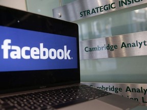 A laptop showing the Facebook logo is held alongside a Cambridge Analytica sign at the entrance to the building housing the offices of Cambridge Analytica, in central London on March 21, 2018.