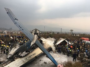 Nepalese rescuers stand near a passenger plane from Bangladesh that crashed at the airport in Kathmandu, Nepal, Monday, March 12, 2018.