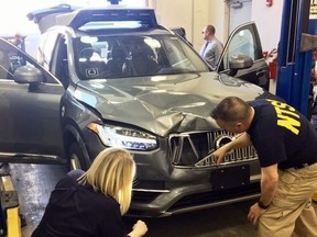 In this March 20, 2018, photo provided by the National Transportation Safety Board, investigators examine a driverless Uber SUV that fatally struck a woman in Tempe, Ariz.  (National Transportation Safety Board via AP)