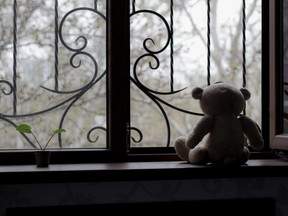 In this stock photo, a teddy bear sits on the windowsill in a dark room.