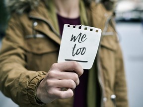 In this stock photo, a young woman in the street holds up a piece of paper with the text me too.